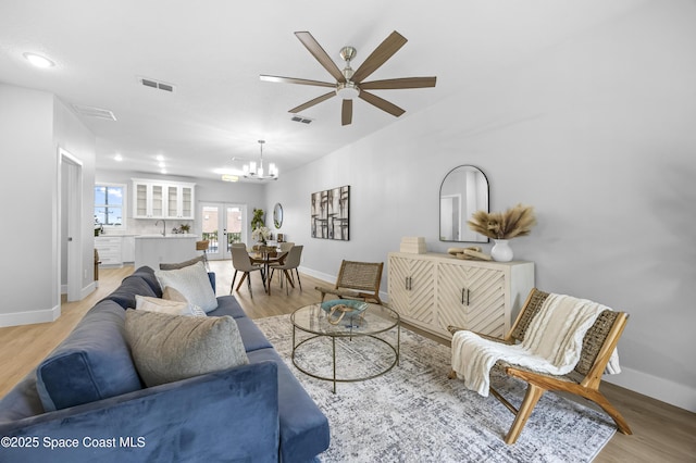 living room with french doors, sink, a notable chandelier, and light hardwood / wood-style flooring