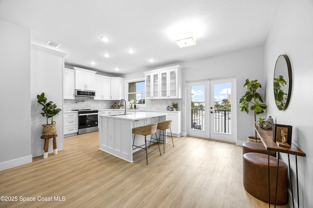 kitchen with french doors, a kitchen bar, white cabinetry, a center island with sink, and stainless steel appliances