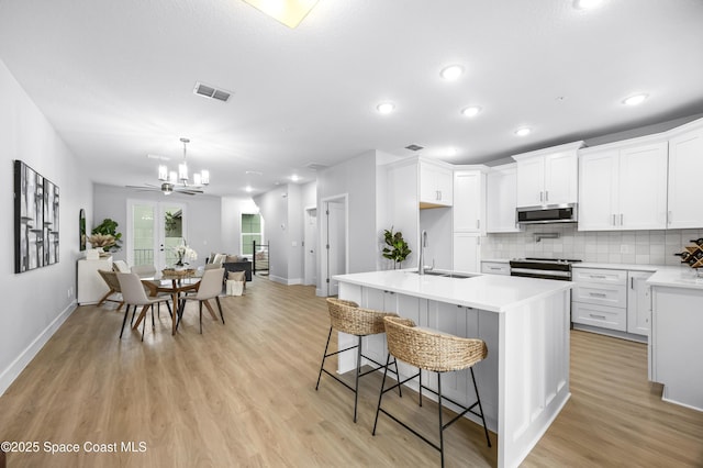 kitchen featuring sink, a kitchen island with sink, white cabinetry, stainless steel appliances, and a kitchen bar