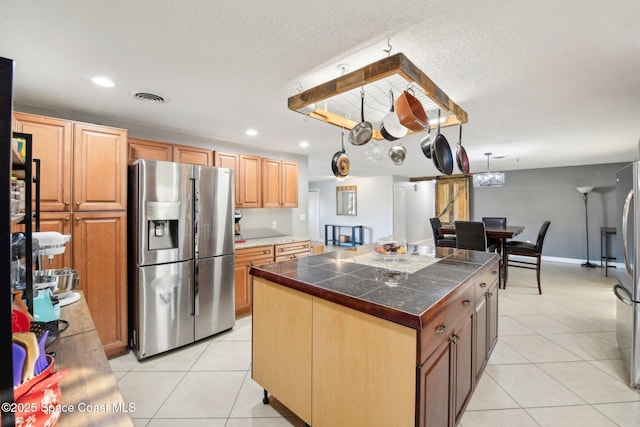 kitchen featuring stainless steel fridge with ice dispenser, light tile patterned floors, a center island, and a textured ceiling