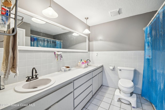 bathroom featuring tile walls, vanity, a textured ceiling, tile patterned floors, and toilet