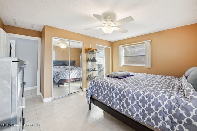 bedroom featuring ceiling fan, multiple closets, a textured ceiling, and light tile patterned flooring