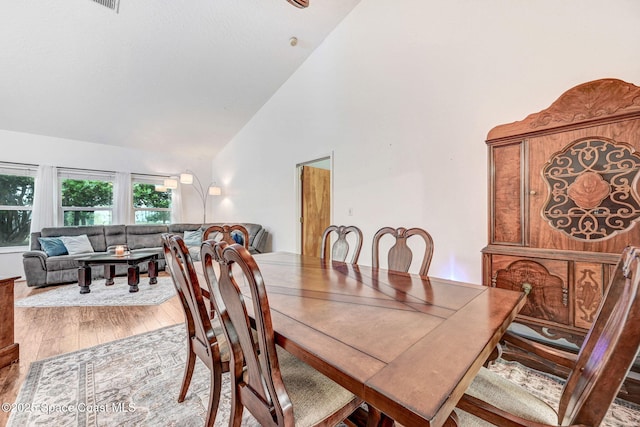 dining room with high vaulted ceiling and light hardwood / wood-style flooring