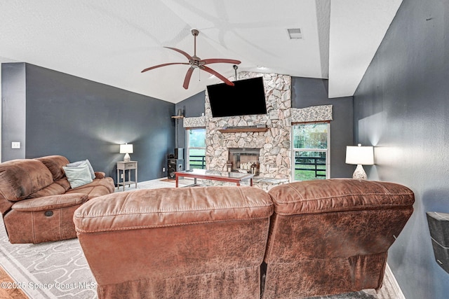 living room featuring ceiling fan, lofted ceiling, and a stone fireplace