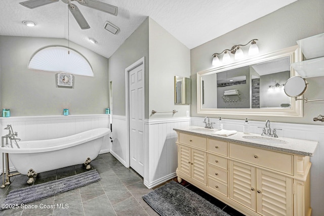 bathroom with lofted ceiling, ceiling fan, a textured ceiling, a bathing tub, and vanity