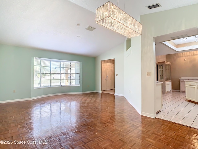 empty room with light parquet floors, an inviting chandelier, and high vaulted ceiling