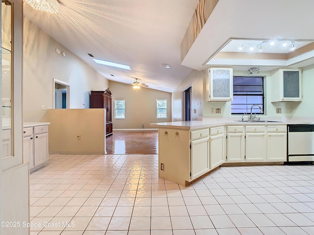 kitchen featuring vaulted ceiling with skylight, dishwasher, sink, light tile patterned floors, and kitchen peninsula