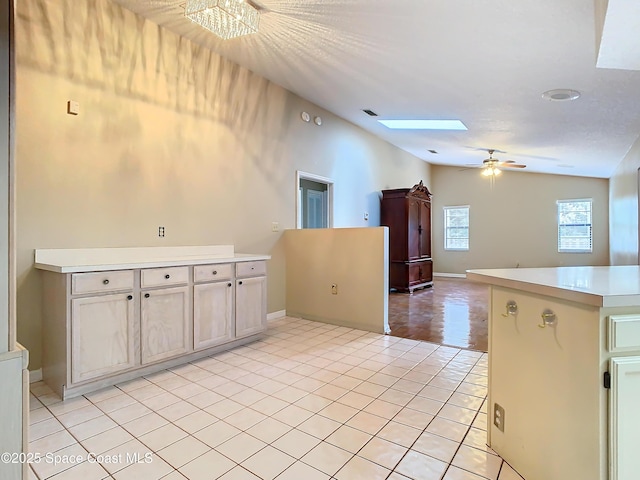 kitchen with light tile patterned flooring, ceiling fan, vaulted ceiling with skylight, and kitchen peninsula