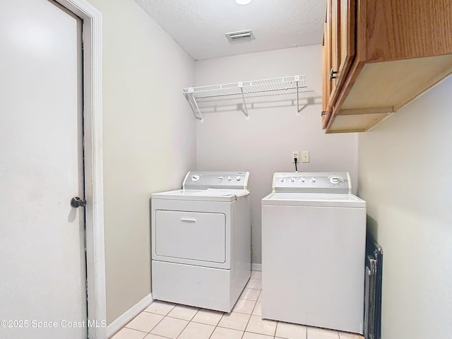 clothes washing area featuring cabinets, washing machine and dryer, light tile patterned flooring, and a textured ceiling