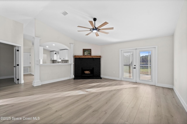 unfurnished living room featuring ceiling fan, a fireplace, vaulted ceiling, french doors, and light wood-type flooring