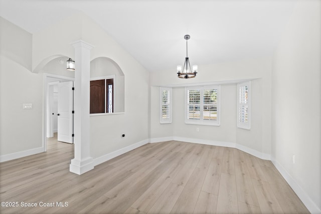 empty room with decorative columns, lofted ceiling, a chandelier, and light hardwood / wood-style flooring