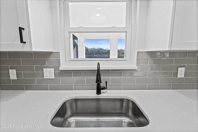 details featuring sink, backsplash, white cabinets, and light stone counters