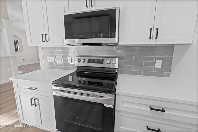 kitchen with white cabinetry, tasteful backsplash, light stone counters, light wood-type flooring, and stainless steel appliances