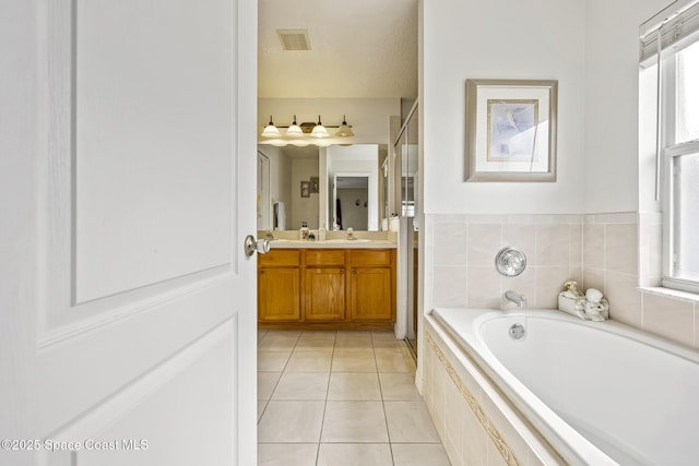 bathroom with a relaxing tiled tub, vanity, tile patterned flooring, and a wealth of natural light