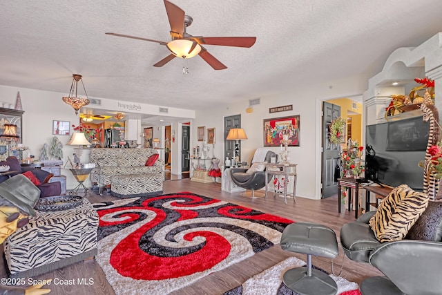 living room featuring hardwood / wood-style flooring, ceiling fan, and a textured ceiling