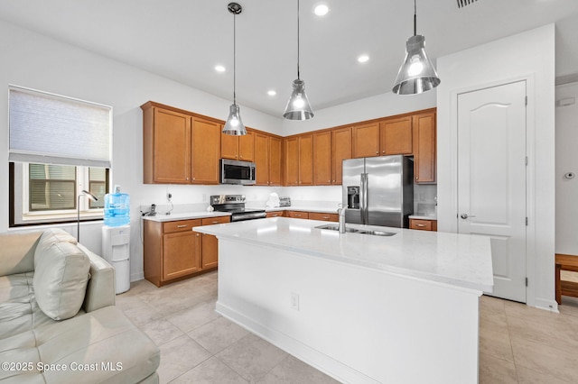 kitchen featuring appliances with stainless steel finishes, sink, hanging light fixtures, light stone counters, and a center island with sink