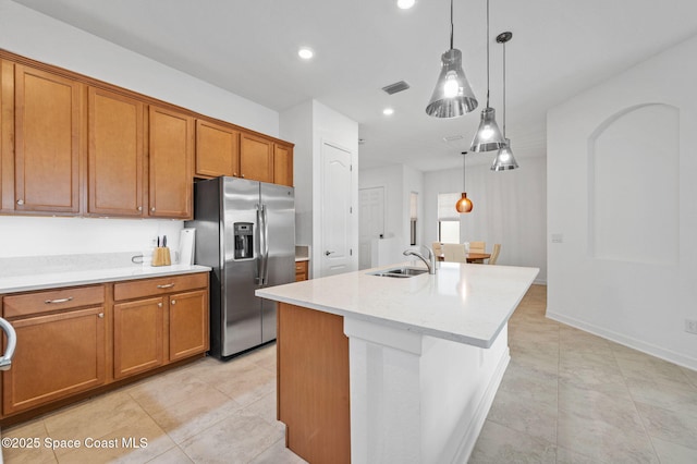 kitchen featuring pendant lighting, an island with sink, sink, light stone counters, and stainless steel refrigerator with ice dispenser