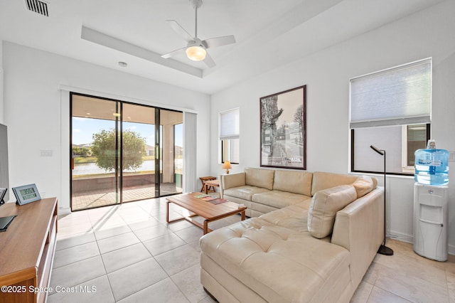 tiled living room with a raised ceiling and ceiling fan