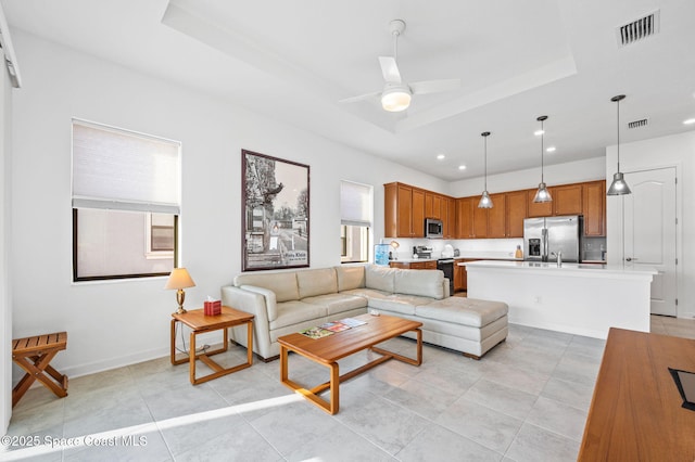 tiled living room featuring sink, ceiling fan, and a tray ceiling