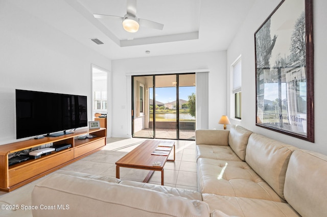 living room with light tile patterned flooring, ceiling fan, and a tray ceiling