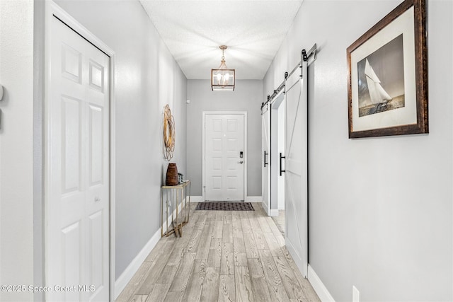 hallway with a barn door, an inviting chandelier, a textured ceiling, and light wood-type flooring