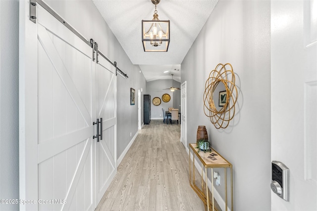 hall featuring a notable chandelier, a barn door, a textured ceiling, and light wood-type flooring