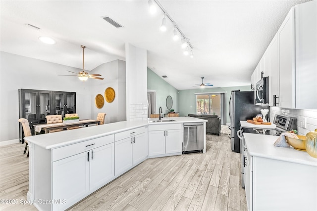 kitchen with lofted ceiling, sink, white cabinetry, stainless steel appliances, and light hardwood / wood-style floors