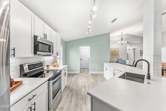 kitchen with vaulted ceiling, appliances with stainless steel finishes, decorative light fixtures, sink, and a barn door