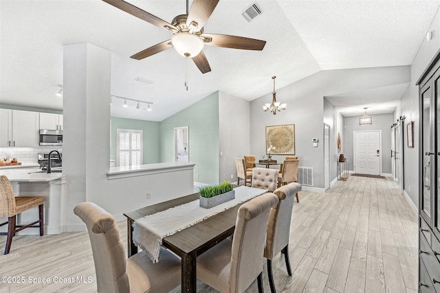 dining space with a textured ceiling, vaulted ceiling, light hardwood / wood-style flooring, and a notable chandelier