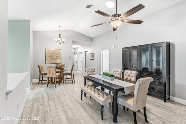 dining room featuring lofted ceiling, ceiling fan with notable chandelier, a barn door, and light wood-type flooring