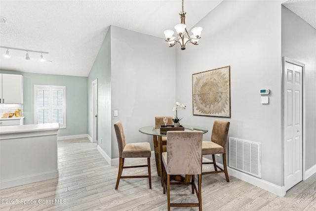 dining area with vaulted ceiling, a textured ceiling, a chandelier, and light hardwood / wood-style flooring