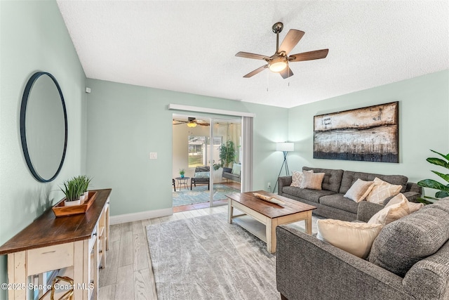 living room with ceiling fan, a textured ceiling, and light wood-type flooring