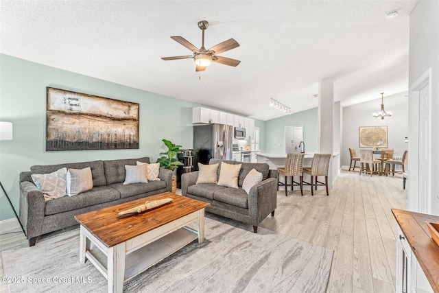 living room featuring vaulted ceiling, ceiling fan with notable chandelier, light hardwood / wood-style floors, and a textured ceiling