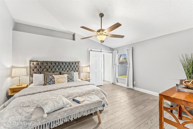 bedroom with ceiling fan, lofted ceiling, a textured ceiling, and light hardwood / wood-style floors