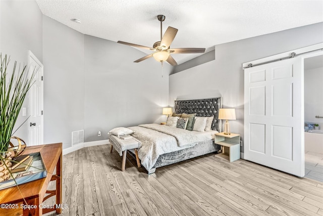 bedroom with ceiling fan, a textured ceiling, vaulted ceiling, a barn door, and light wood-type flooring