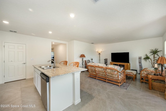 kitchen with sink, dishwasher, white cabinetry, light stone countertops, and an island with sink