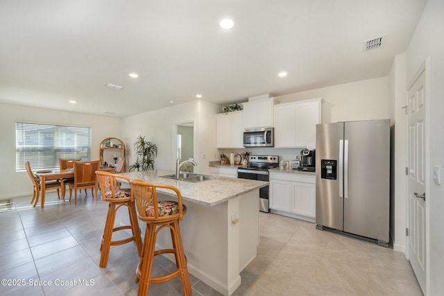 kitchen featuring sink, appliances with stainless steel finishes, light stone counters, white cabinets, and a center island with sink