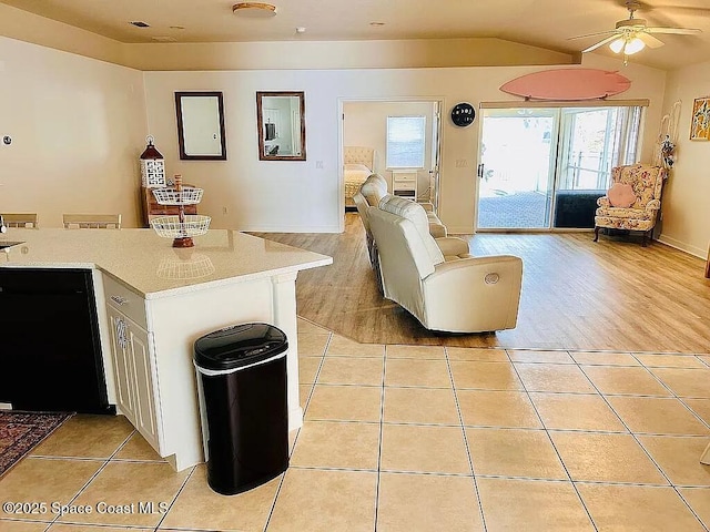 kitchen with white cabinetry, vaulted ceiling, black dishwasher, and light tile patterned flooring