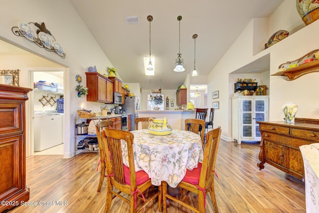 dining room featuring washing machine and clothes dryer, high vaulted ceiling, and light hardwood / wood-style floors