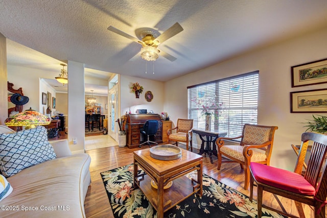 living room with ceiling fan with notable chandelier, a textured ceiling, and light wood-type flooring