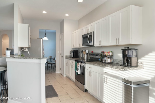 kitchen featuring light stone countertops, appliances with stainless steel finishes, a breakfast bar area, and white cabinets