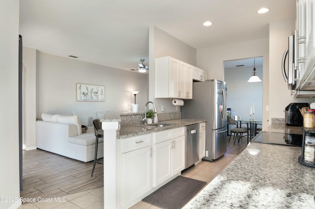 kitchen featuring sink, appliances with stainless steel finishes, light stone countertops, white cabinets, and decorative light fixtures