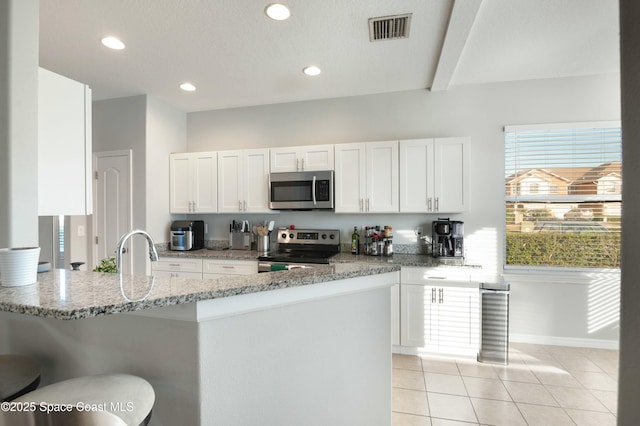 kitchen featuring a breakfast bar area, appliances with stainless steel finishes, white cabinetry, light stone counters, and kitchen peninsula