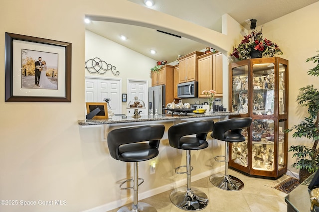 kitchen with lofted ceiling, light tile patterned floors, stainless steel appliances, light stone counters, and a kitchen bar