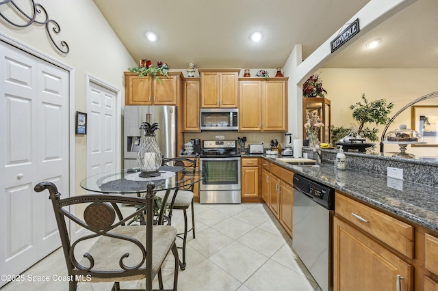 kitchen with light tile patterned flooring, stainless steel appliances, sink, and dark stone countertops