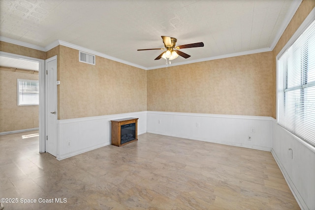 unfurnished room featuring ceiling fan, wainscoting, a glass covered fireplace, and crown molding