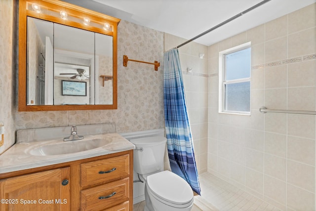 bathroom featuring wallpapered walls, toilet, vanity, a tile shower, and ceiling fan