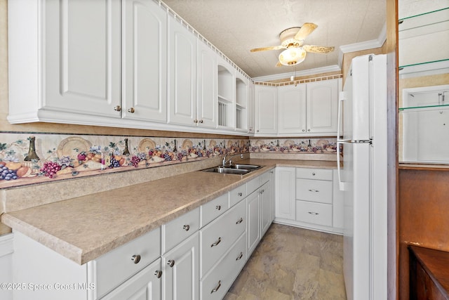 kitchen with a sink, freestanding refrigerator, white cabinets, light countertops, and ceiling fan