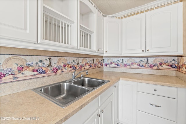 kitchen with a sink, white cabinets, light countertops, and glass insert cabinets