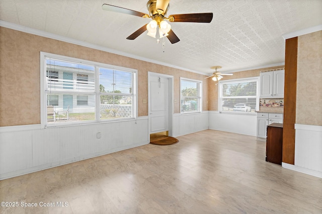unfurnished room featuring a wainscoted wall, ceiling fan, an ornate ceiling, light wood-type flooring, and crown molding